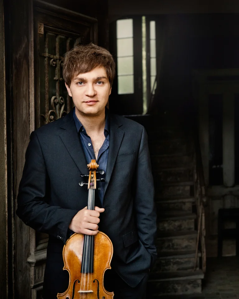 Nils Mönkemeyer: Ein Mann in einem Anzug steht in einem dunklen Raum und hält eine Geige. Im Hintergrund eine Treppe.