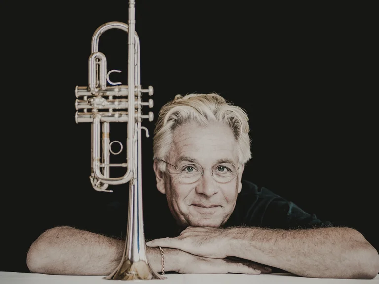 Håkan Hardenberger: Ein Mann mit grauen Haaren lehnt sich auf ein weißes Podest, eine Trompete steht neben ihm aufrecht.