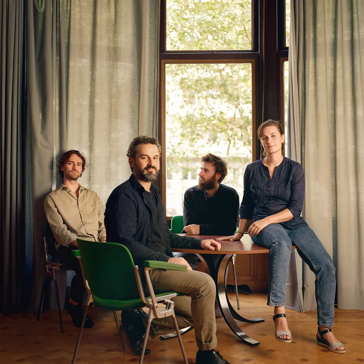 Nevermind: Vier Personen sitzen lässig in einem Raum mit Holzboden und großen Fenstern. Sie blicken ruhig in die Kamera.