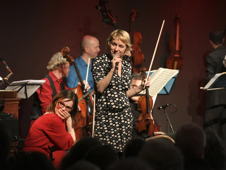 Ensemble Resonanz: Eine Sängerin in einem gepunkteten Kleid singt auf einer Bühne, begleitet von mehreren Musikern, die klassische Instrumente spielen.